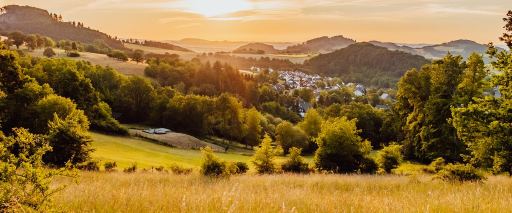 Hallenberg Eine Landschaft aus Wiesen und Wäldern mit ein paar Häusern und Blick auf einen der Trekkingplätze zum zelten in der untergehenden Abendsonne.