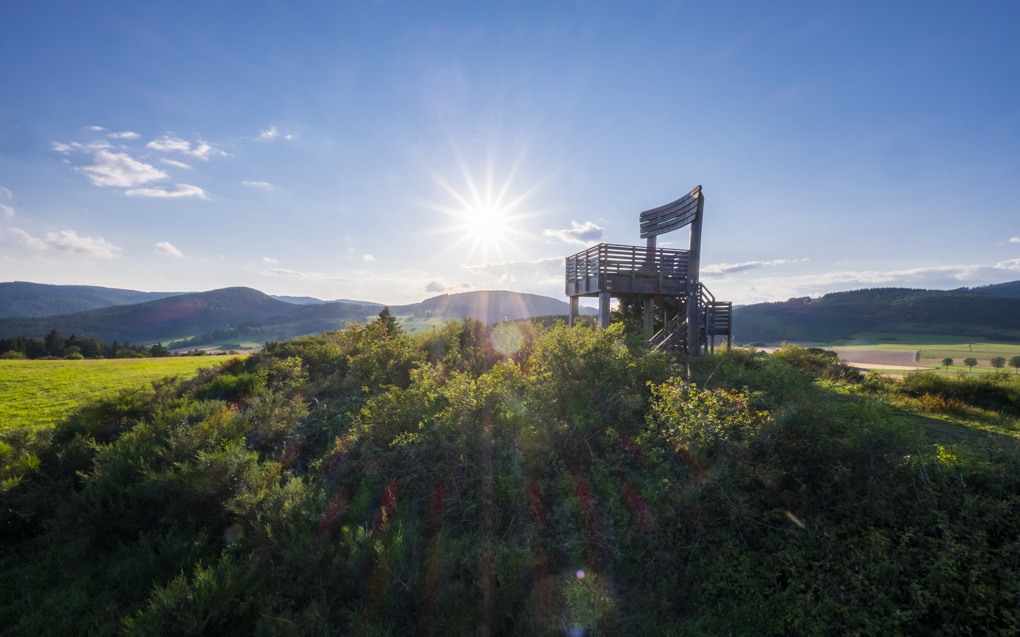 Der Aussichtsturm Sauerland Stabil Stuhl, ein großer Stuhl aus Holz, inmitten von Wäldern und Wiesen.