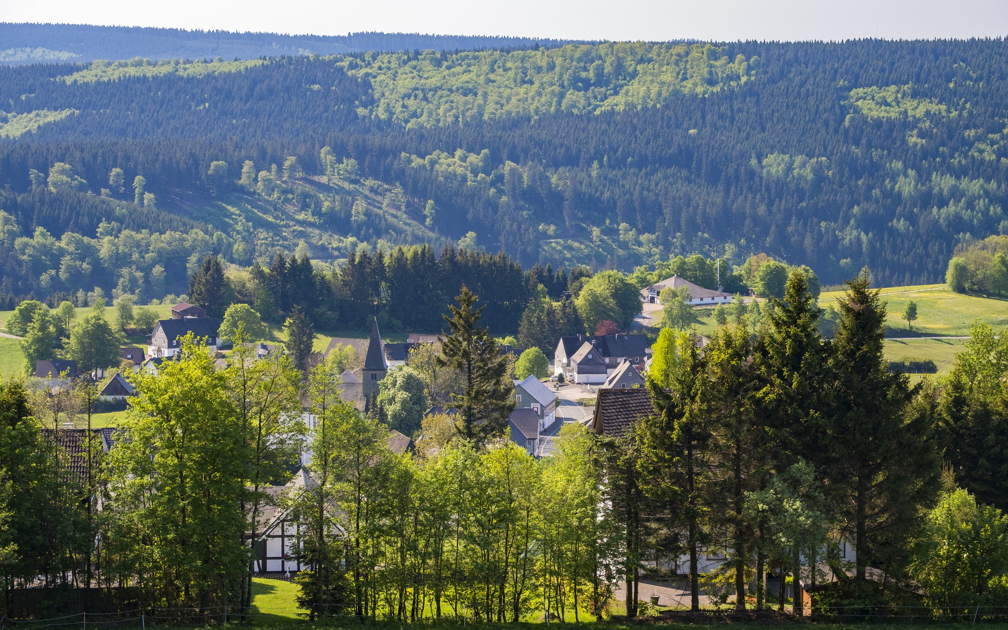 FerienweltWinterberg_2018_Neuastenberg_Ortsansicht_Weitblick_Sommer Ein Teil der Ortschaft Neuastenberg inmitten von Wäldern und Wiesen.