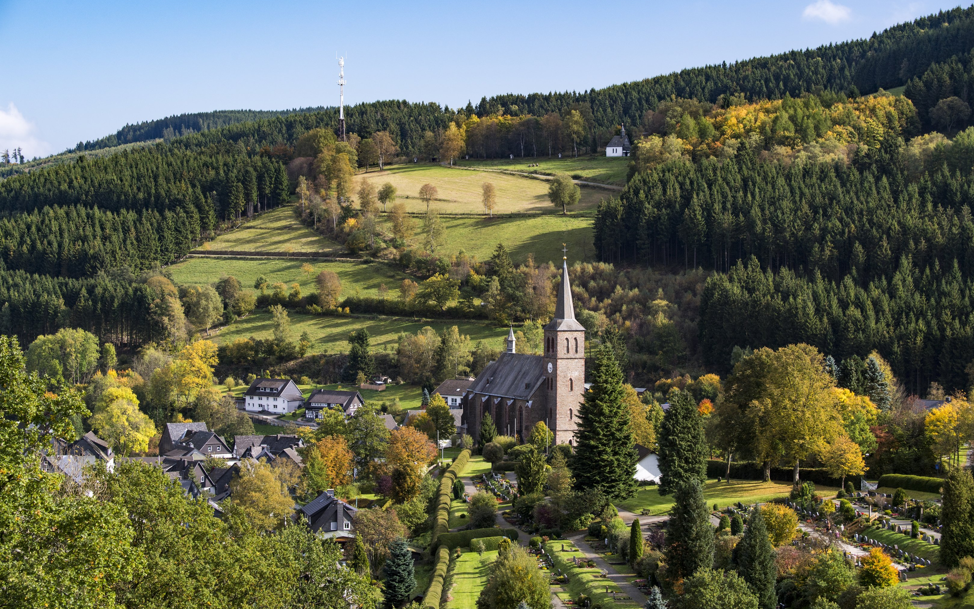 FerienweltWinterberg_Zueschen_Landschaft_Ort_Kirche_Herbst Blick auf die Ortschaft Züschen mit Kirchturm umgeben von Wäldern und Bergen.