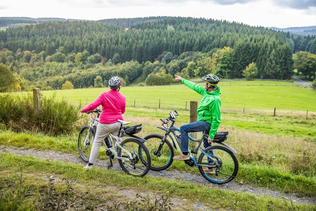 Ein Mann und eine Frau auf E-Bikes, die gerade eine Pause machen, während der Mann auf etwas in der Ferne zeigt.