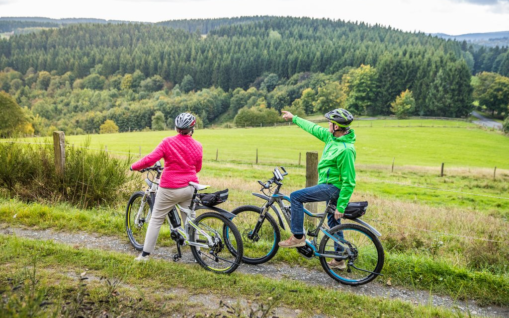 Ein Mann und eine Frau auf E-Bikes, die gerade eine Pause machen, während der Mann auf etwas in der Ferne zeigt.