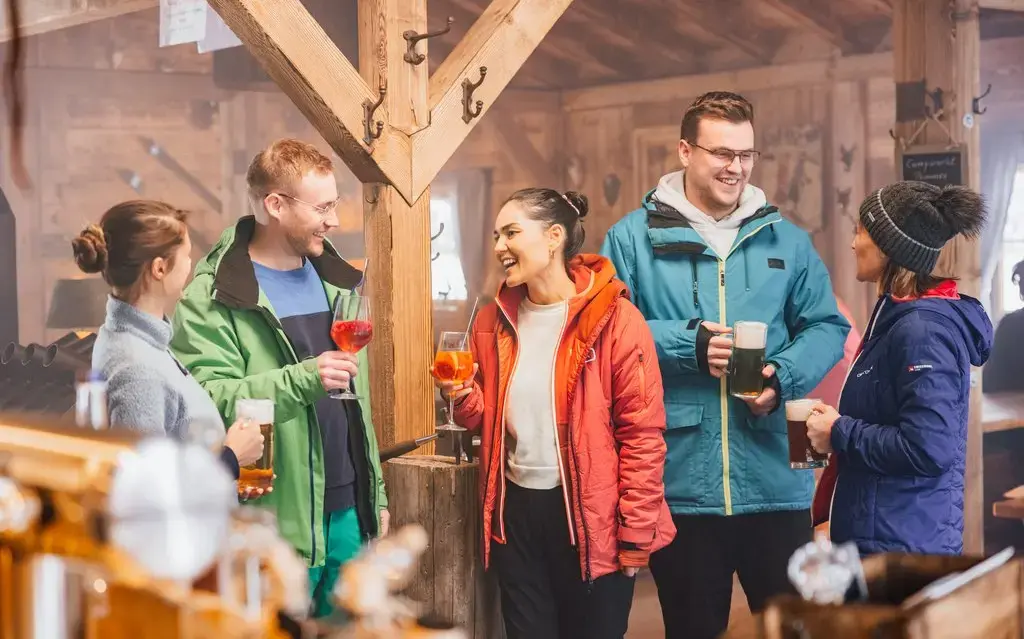 Eine Gruppe Freunde, die mit Getränken in einer Hütte steht und sich unterhält und lacht.