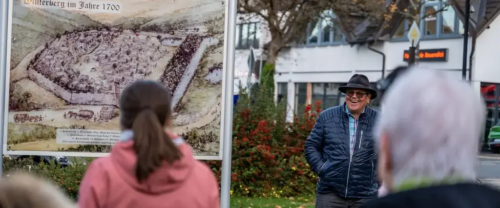 Der Altstadtführer erklärt einer Gruppe etwas auf einer Tafel auf welcher ein Bild von Winterberg im Jahre 1700 zu sehen ist.