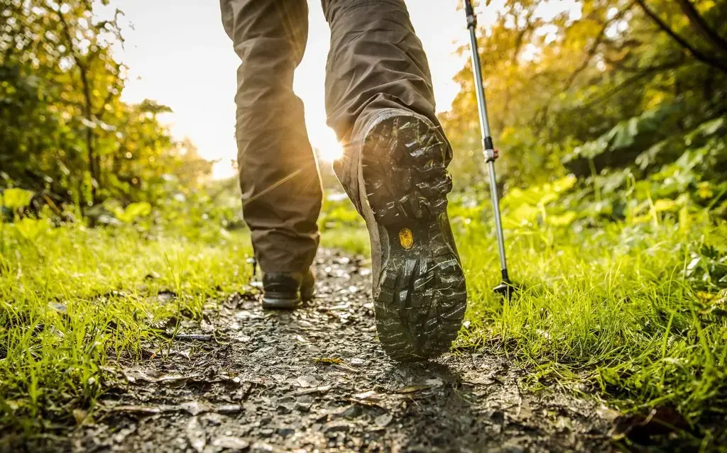 Ein paar Beine mit Wanderschuhen, die einen Waldweg entlang wandern.