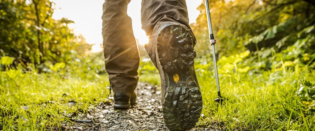 Ein paar Beine mit Wanderschuhen, die einen Waldweg entlang wandern.