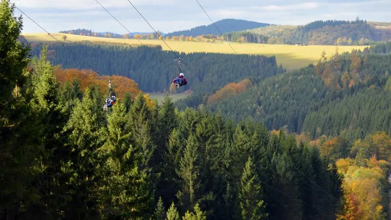 Zwei Personen fliegen in ihren Gurten die Megazipline Astenkick herunter.