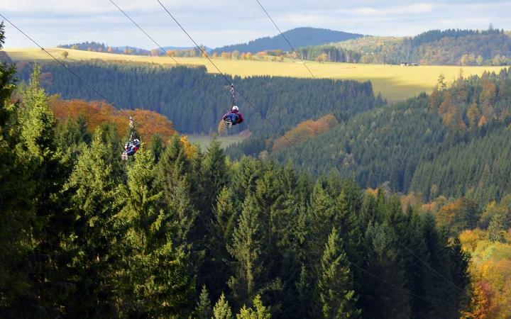 Zwei Personen fliegen in ihren Gurten die Megazipline Astenkick herunter.