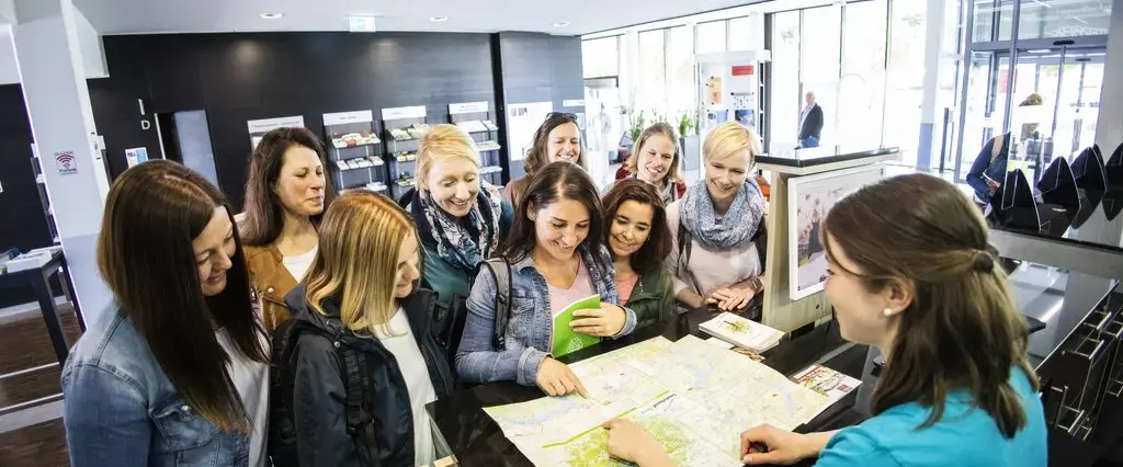 Eine Mitarbeiterin der Tourist Information erklärt einer Gruppe von Frauen etwas auf einer Karte.