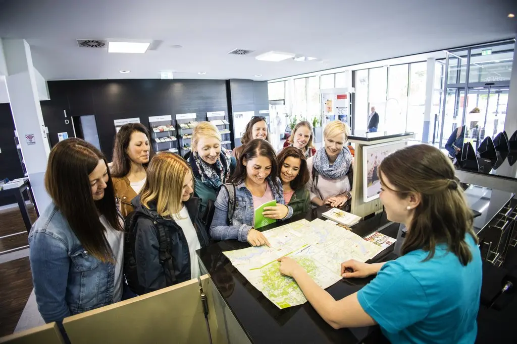 Eine Mitarbeiterin der Tourist Information erklärt einer Gruppe von Frauen etwas auf einer Karte.