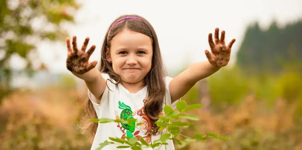 Ein kleines Mädchen streckt ihre mit Erde verdreckten Hände in die Luft, mit denen sie gerade erst einen neuen Baum eingepflanzt hat.