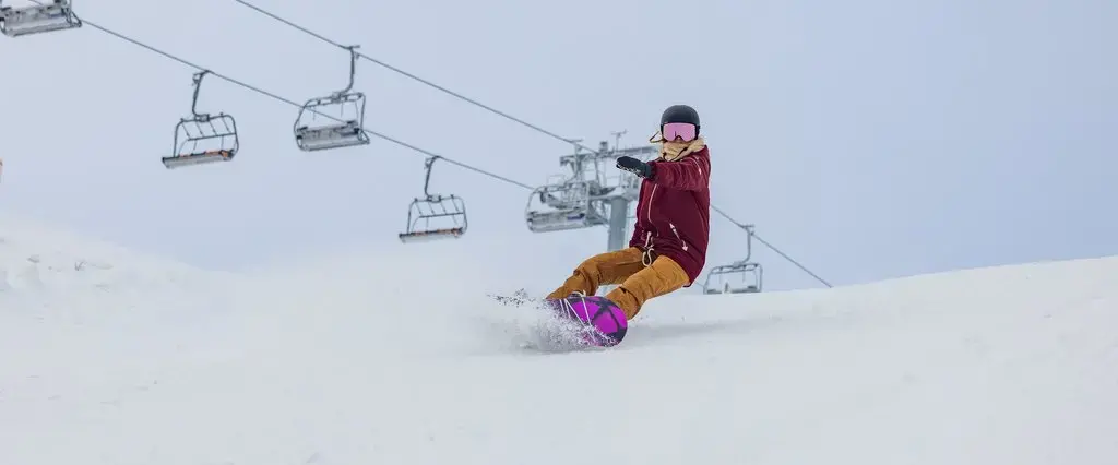 Ein Snowboardfahrer fährt auf seinem Snowboard einen Skihang hinunter.