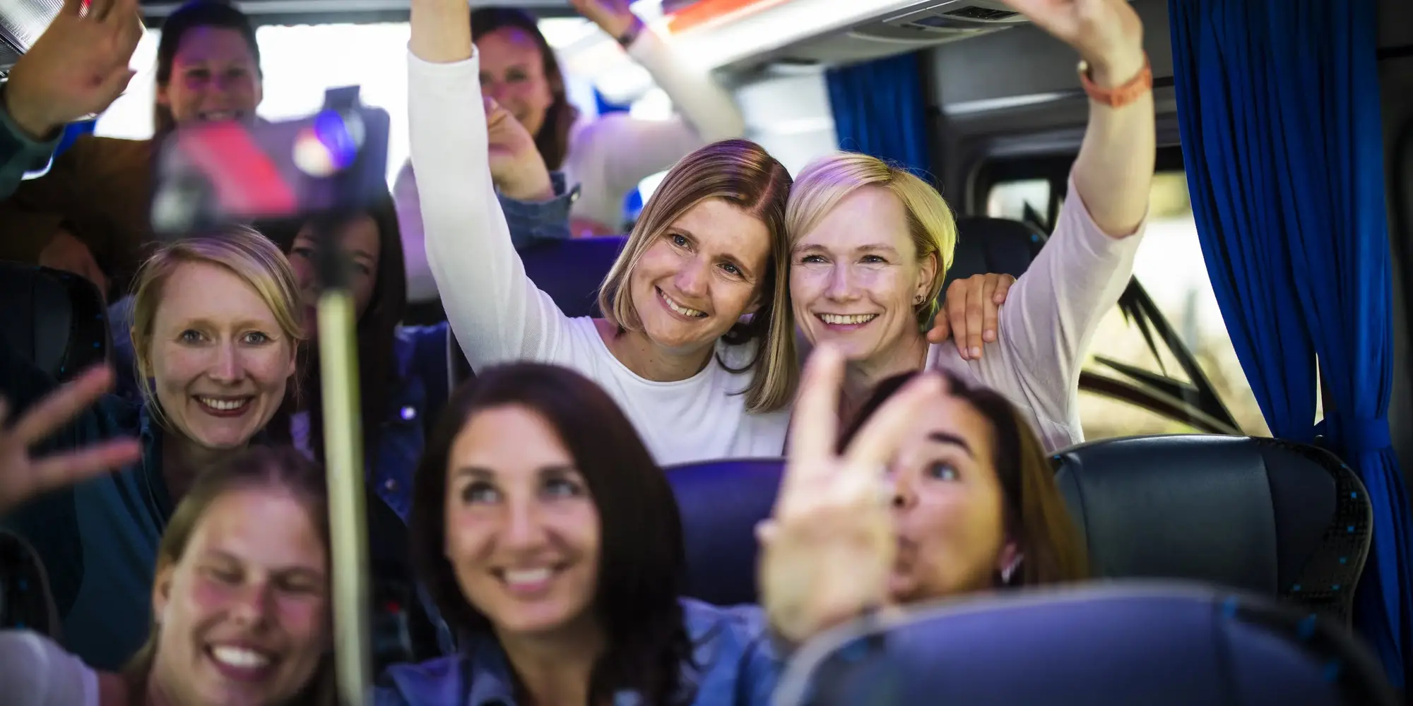 Mehrere Frauen, die im Bus sitzen und lächelnd mit den Fingern das Peace-Zeichen in Richtung kamera machen.