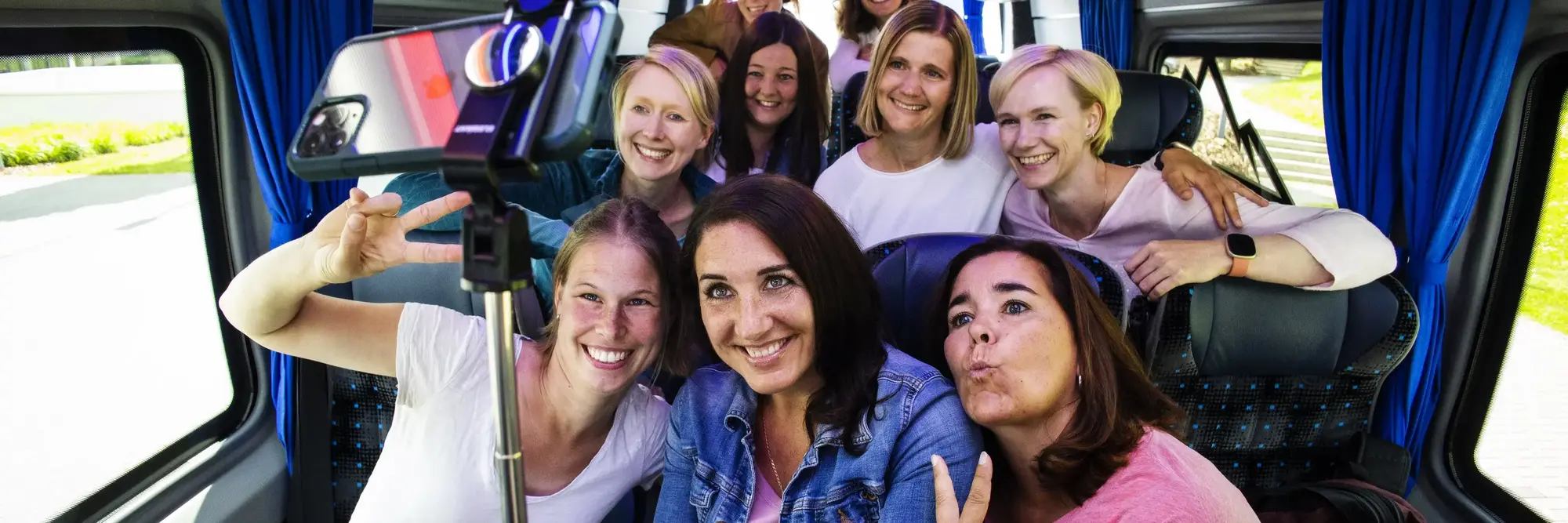 Mehrere Frauen, die in einem kleinen Bus sitzen und ein gemeinsames Selfie mit einem Selfiestick machen.