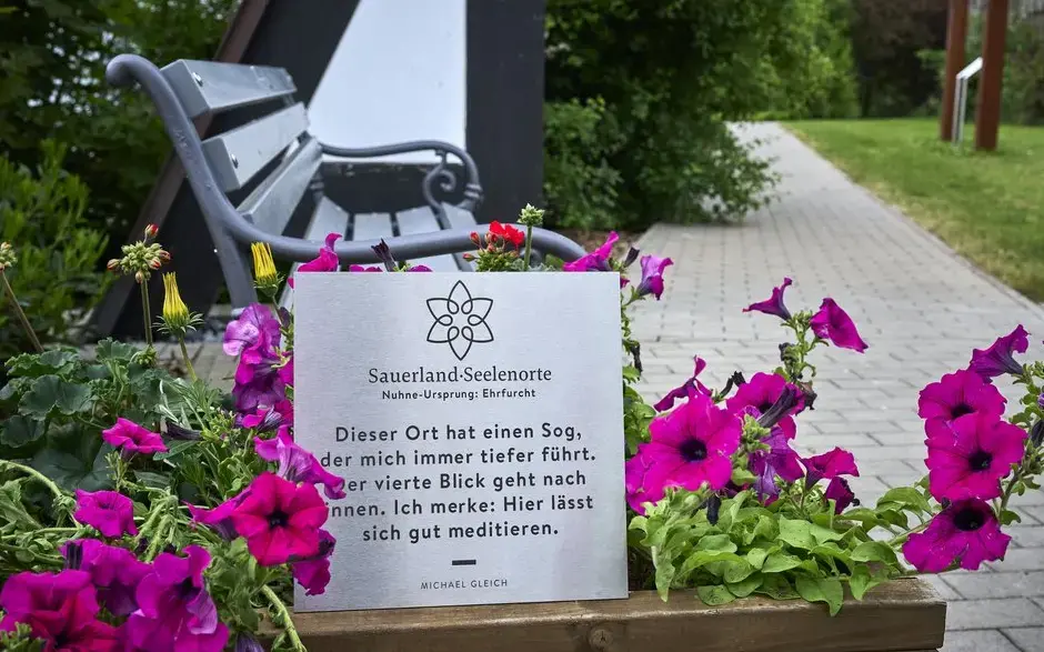 Ein Schild vor einer Bank mit der Aufschrift Sauerland Seelenorte Nuhne-Ursprung Erfurcht. Dieser Ort hat einen Sog, der mich immer tiefer führt, der vierte Blick geht nach innen. Ich merke: hier lässt sich gut meditieren.