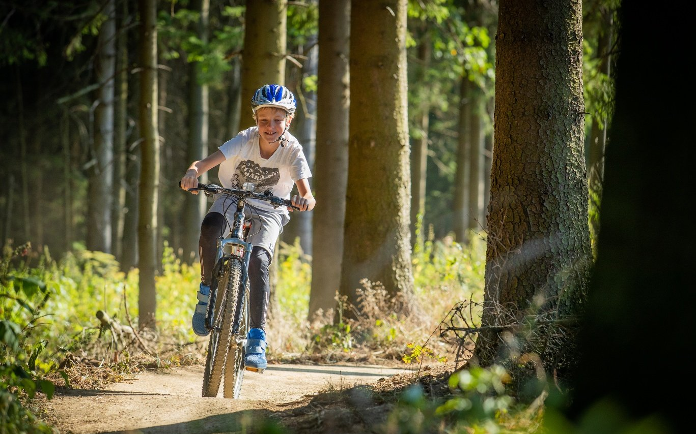 Ein Kind fährt auf seinem Fahrrad einen Trail des Trailparks durch den Wald entlang.