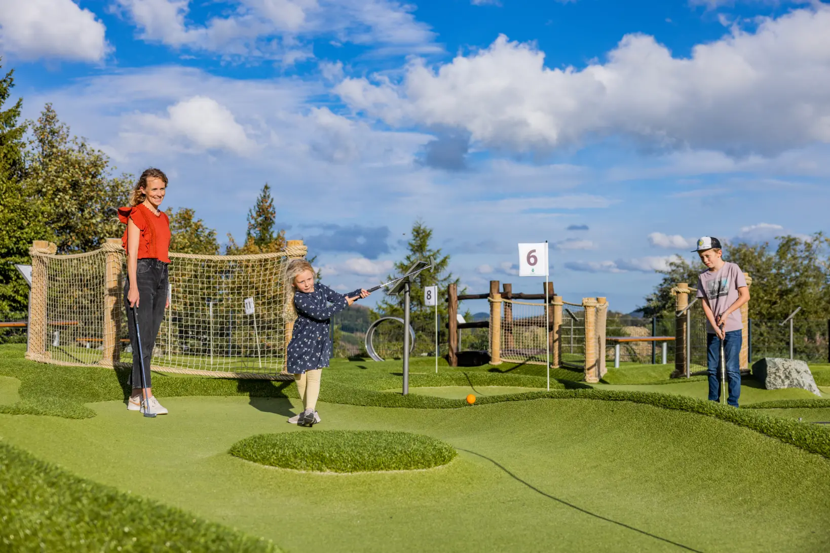 Eine Mutter mit zwei Kindern beim Golf spielen auf der Adventuregolf Anlage.