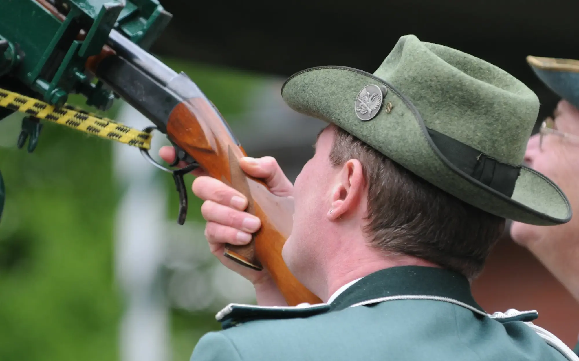 Ein Mann mit Schützenhut und Uniform beim Zielen mit einem Gewehr.