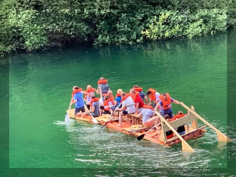 Eine Gruppe die auf einem selbstgebautem Floß über das Wasser fahren.