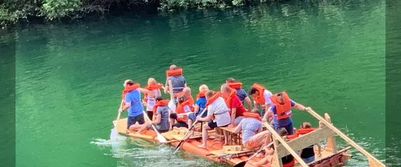 Eine Gruppe die auf einem selbstgebautem Floß über das Wasser fahren.