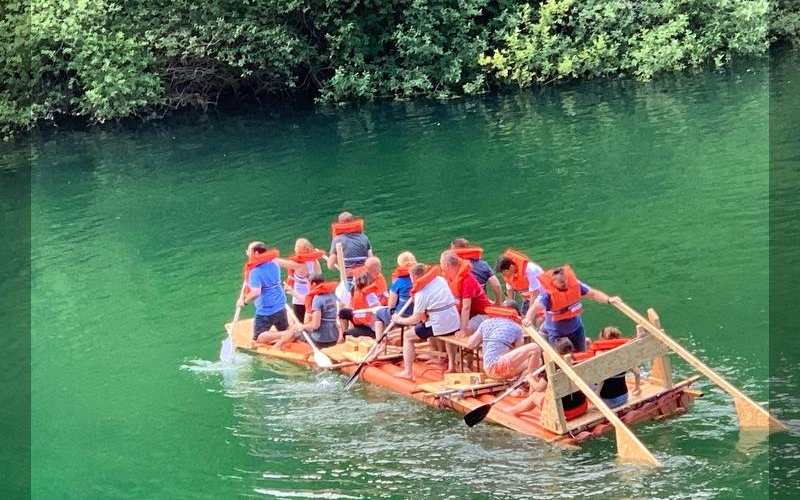 Eine Gruppe die auf einem selbstgebautem Floß über das Wasser fahren.