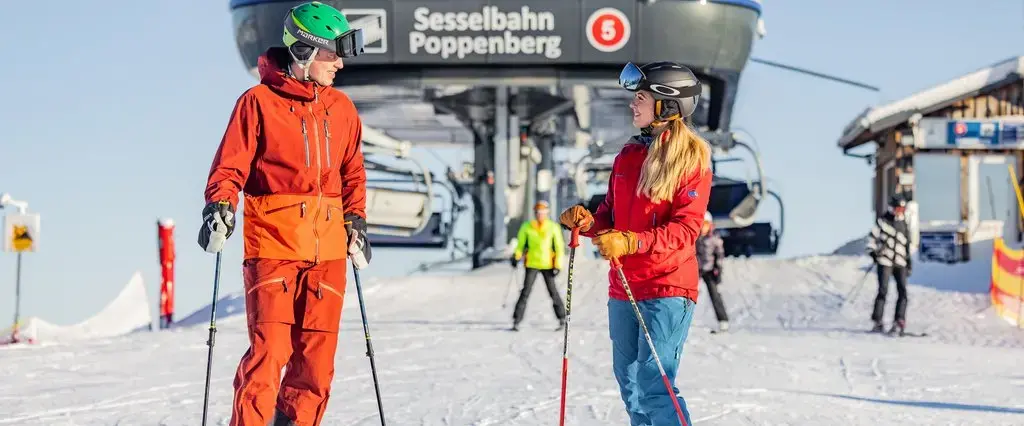 Zwei Skifahrer stehen vor dem Ausstieg eines Sesselliftes und schauen sich an.
