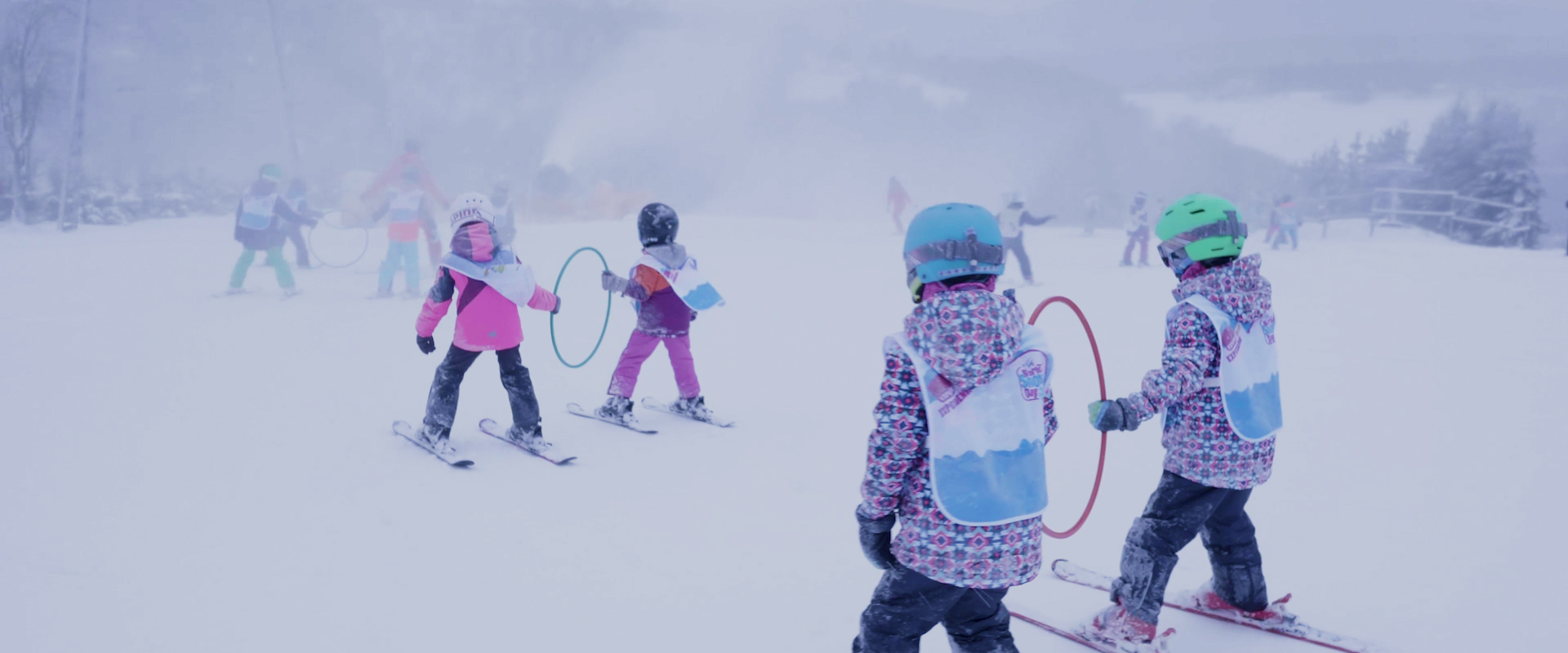 Mehrere Kinder beim Skifahren üben, die immer zu zweit einen Reifen zwischen sich halten.