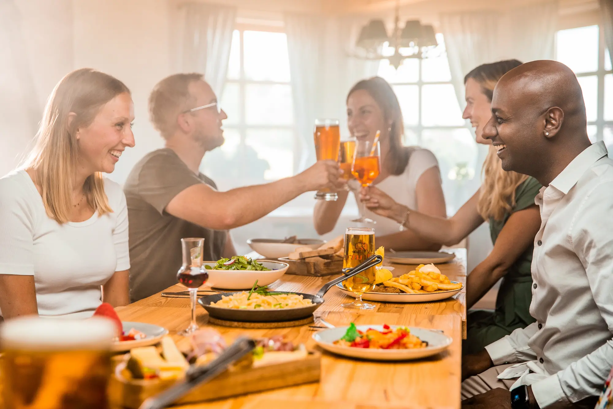 Gruppe von Freunden beim gemeinsamen Essen und Trinken in einer rustikalen Skihütte.