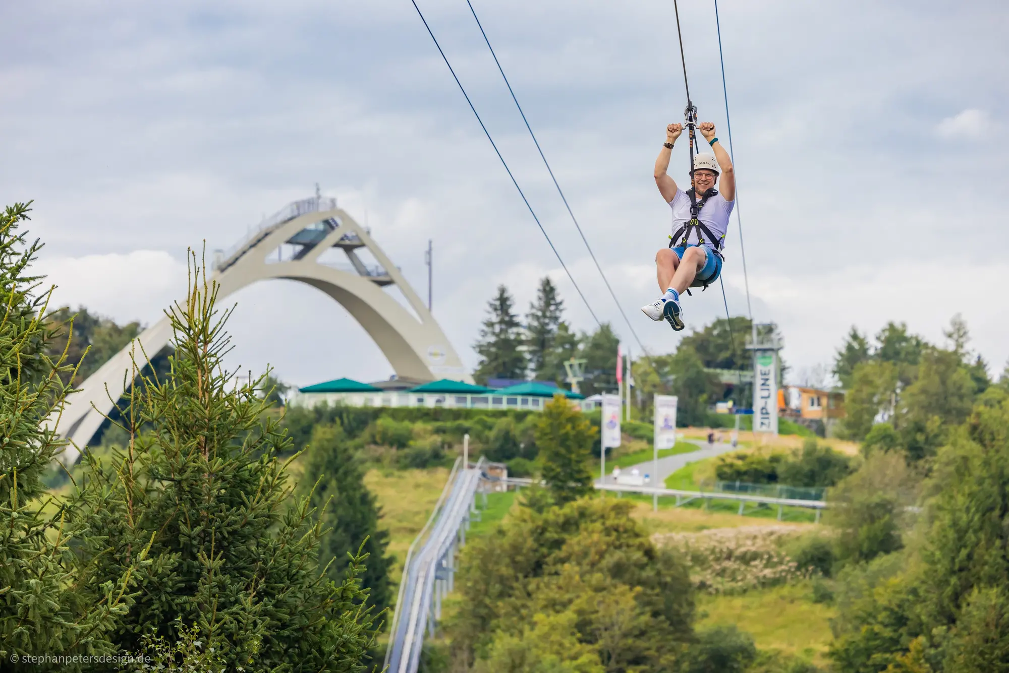 Ein Mann fliegt im Vordergrund der St. Georg Schanze die Zipline hinunter.