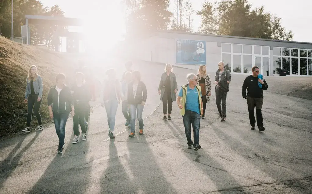 Eine Gruppe aus Männern und Frauen läuft hingter dem Bobbahnführer her.