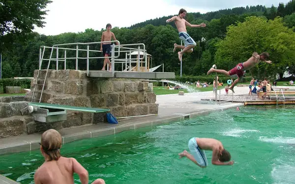 Mehrere Kinder schwimmen im Schwimmbecken oder springen vom Sprungbrett ins Wasser.