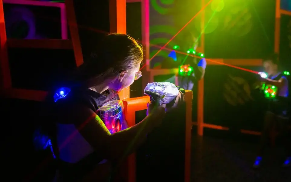 Zwei Frauen halten Laserpistolen in der Hand und versuchen sich gegenseitig im dunklen Raum mit den Lasern zu treffen.