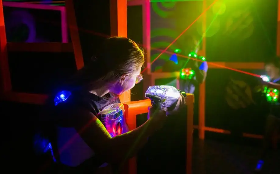 Zwei Frauen halten Laserpistolen in der Hand und versuchen sich gegenseitig im dunklen Raum mit den Lasern zu treffen.