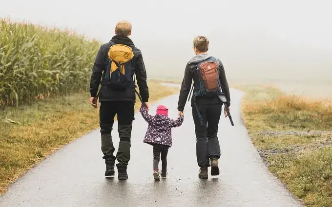 Ein Kind hält Mutter und Vater an den Händen und sie wandern einen Feldweg entlang.