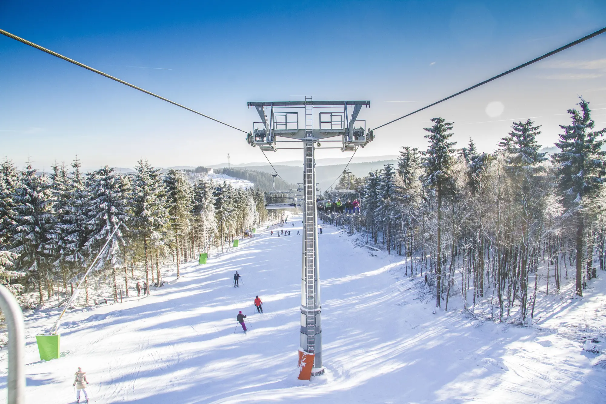 Ein Sessellift, der über einen Skihang mit Ski- und Snowboardfahrern hinwegfährt.