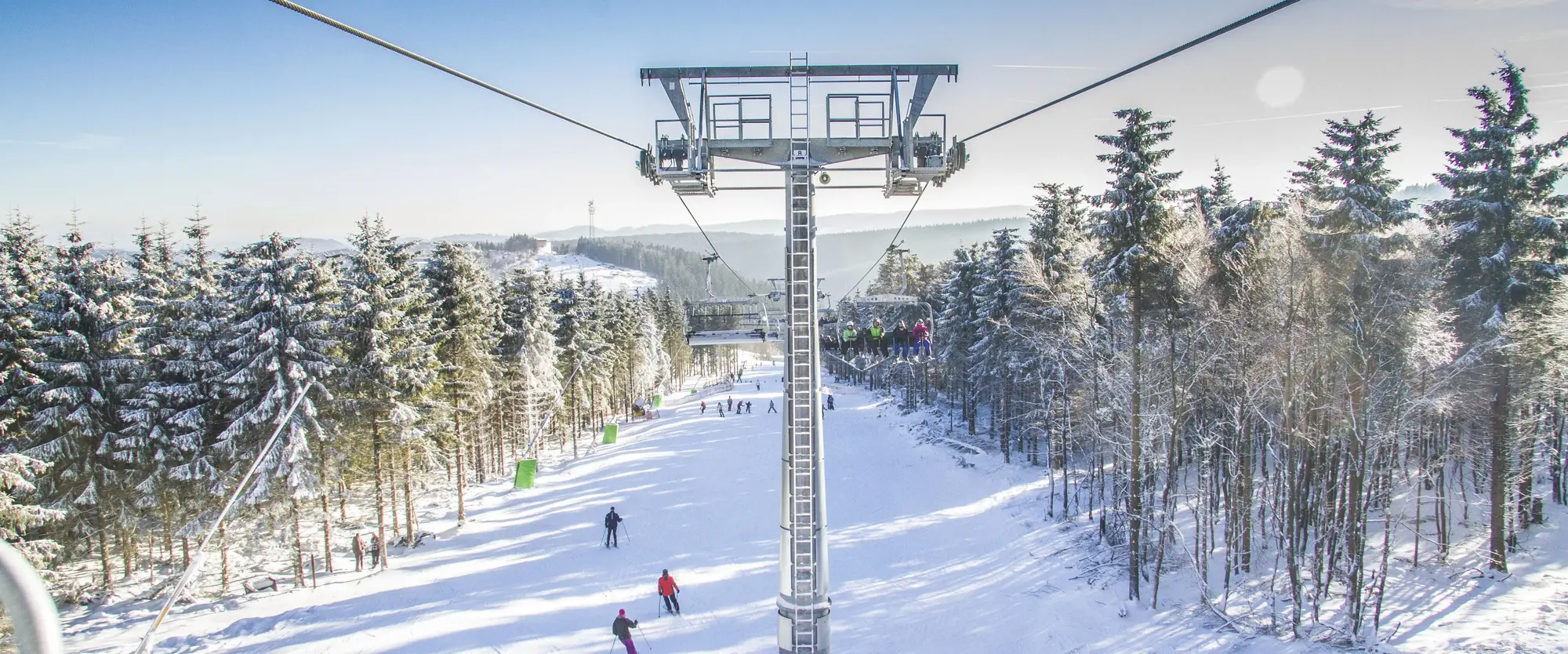 Ein Sessellift, der über einen Skihang mit Ski- und Snowboardfahrern hinwegfährt.