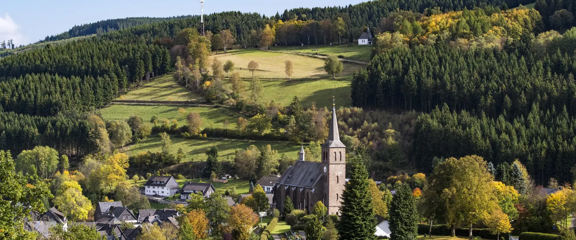 Blick auf die Ortschaft Züschen mit Kirchturm umgeben von Wäldern und Bergen.